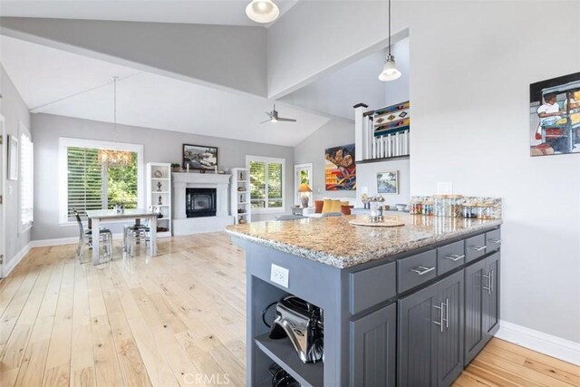 kitchen featuring pendant lighting, vaulted ceiling, light stone countertops, and a healthy amount of sunlight