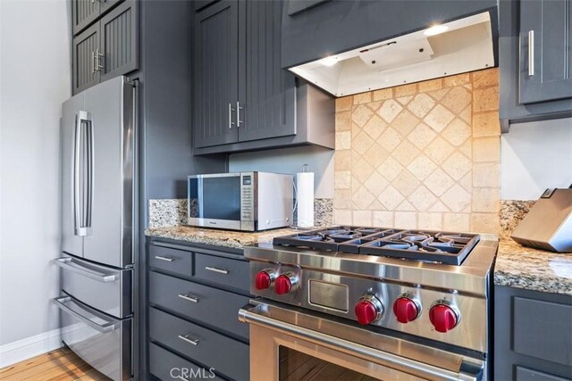 kitchen with light stone counters, ventilation hood, appliances with stainless steel finishes, hardwood / wood-style flooring, and decorative backsplash