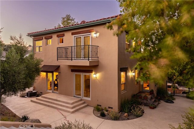 back house at dusk with a fire pit, central AC, a patio, and a balcony