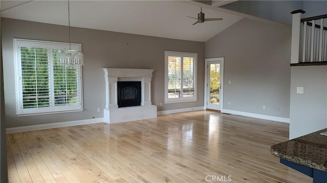 unfurnished living room with ceiling fan with notable chandelier, light hardwood / wood-style floors, and a healthy amount of sunlight