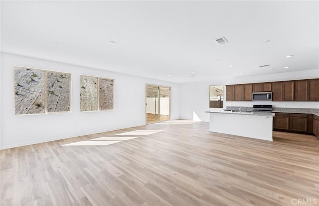 kitchen with open floor plan, light wood-style flooring, stainless steel microwave, and visible vents