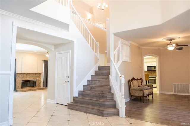 stairway with a high end fireplace, hardwood / wood-style floors, ceiling fan with notable chandelier, and crown molding