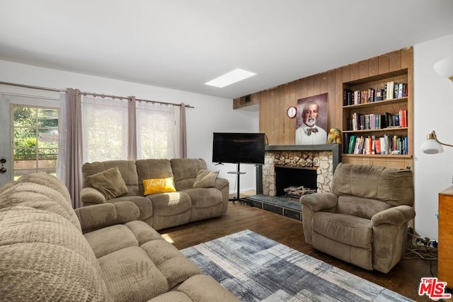 living room featuring dark hardwood / wood-style flooring, a stone fireplace, and wooden walls