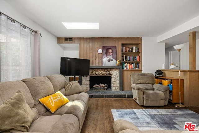 living room featuring dark hardwood / wood-style floors, a stone fireplace, and built in features