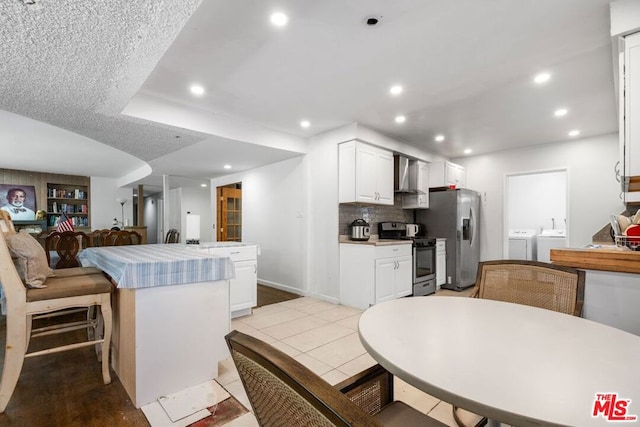 kitchen with appliances with stainless steel finishes, wall chimney exhaust hood, a textured ceiling, washing machine and clothes dryer, and white cabinets