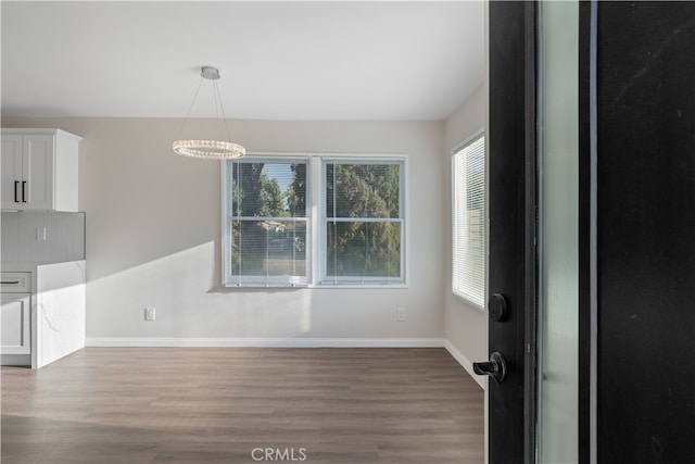 unfurnished dining area with wood-type flooring and a notable chandelier