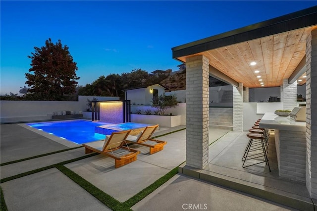 pool at dusk featuring a patio area and an outdoor bar