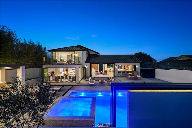 pool at dusk featuring an in ground hot tub and a patio