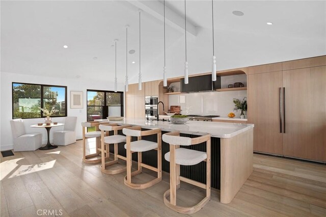 kitchen featuring decorative light fixtures, beamed ceiling, light stone counters, and a center island with sink