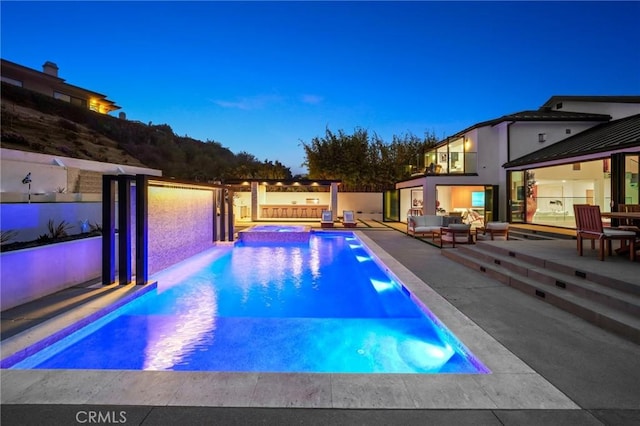 pool at dusk with outdoor lounge area, an in ground hot tub, and a patio