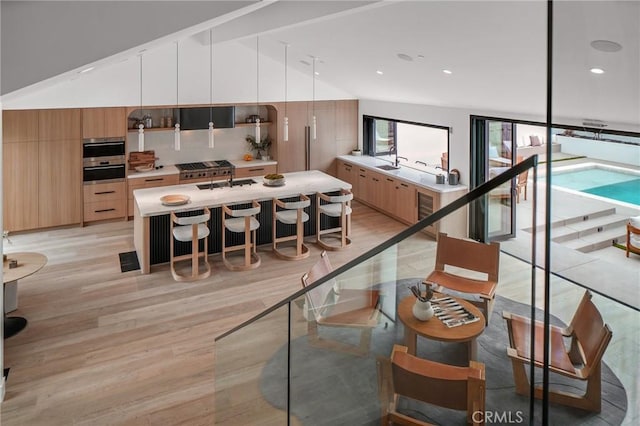 kitchen featuring light hardwood / wood-style floors, a center island with sink, a kitchen bar, backsplash, and lofted ceiling