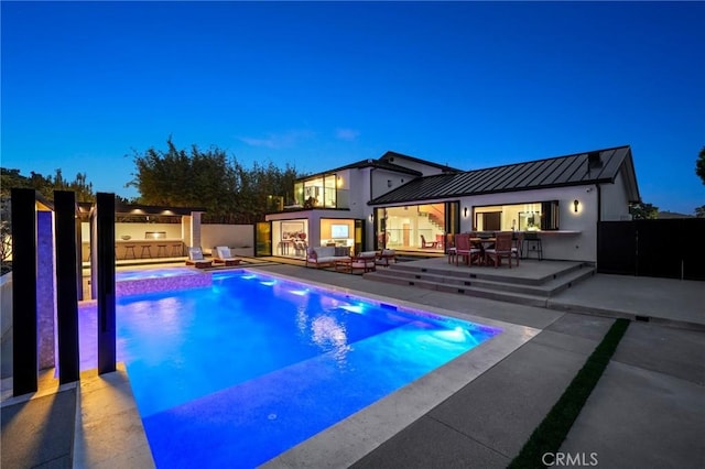 pool at dusk featuring a patio area and an in ground hot tub