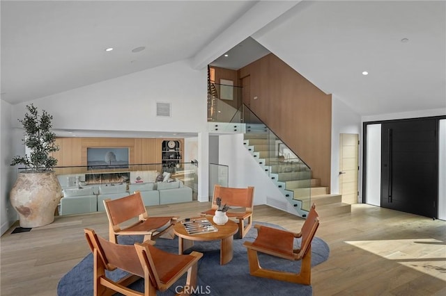 living room with high vaulted ceiling, light hardwood / wood-style flooring, and beamed ceiling