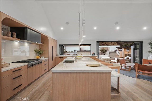 kitchen featuring a large island with sink, sink, hanging light fixtures, stainless steel gas cooktop, and light stone counters