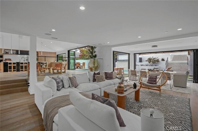 living room featuring vaulted ceiling, sink, and light hardwood / wood-style flooring