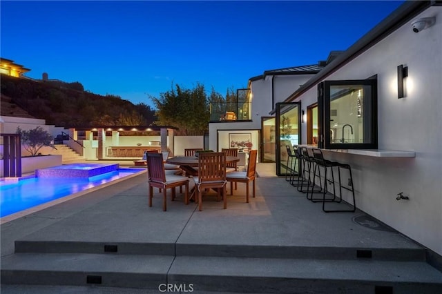 patio terrace at dusk with a pool with hot tub and exterior bar