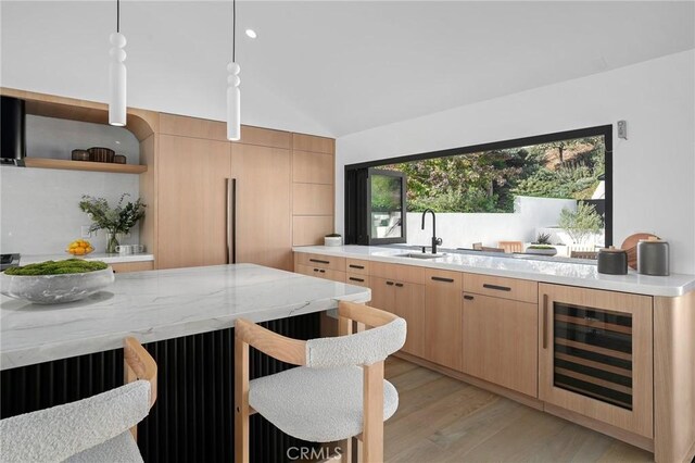 kitchen with decorative light fixtures, wine cooler, sink, light brown cabinetry, and light stone counters