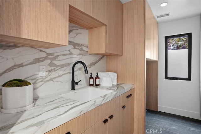 bar with decorative backsplash, light stone counters, sink, and light brown cabinets