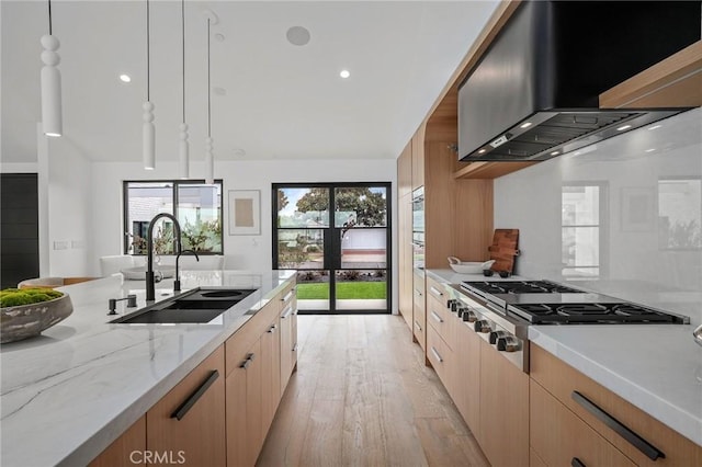 kitchen featuring decorative light fixtures, stainless steel gas cooktop, wall chimney exhaust hood, light stone counters, and sink