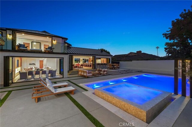 pool at dusk with an outdoor hangout area, a patio, and an in ground hot tub