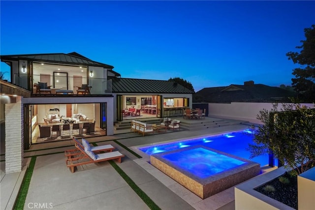 pool at dusk featuring an outdoor hangout area, a patio area, and an in ground hot tub