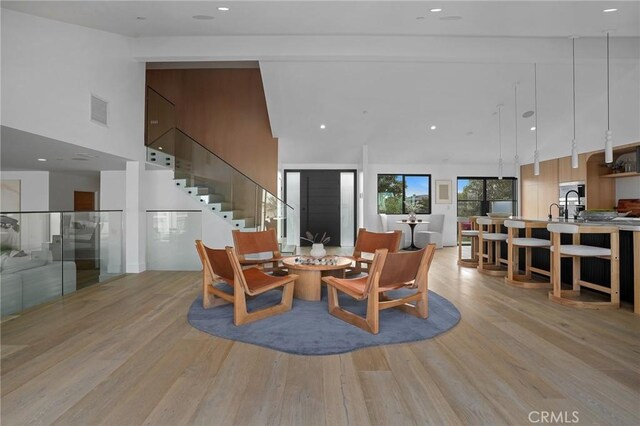 living room featuring a towering ceiling, sink, and light hardwood / wood-style floors