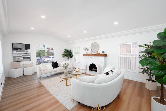 living room with ornamental molding, light wood-type flooring, vaulted ceiling, and a high end fireplace