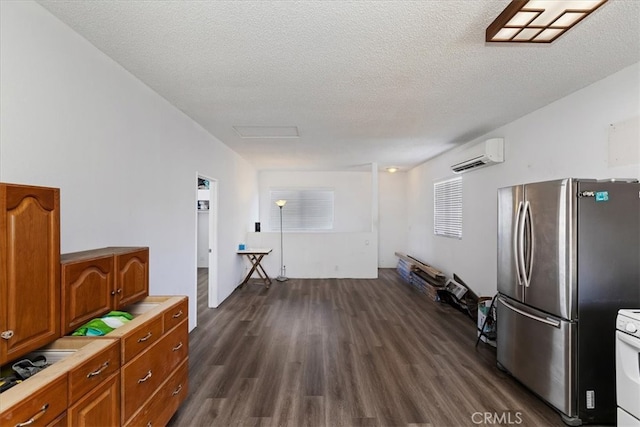 kitchen with a textured ceiling, a wall mounted AC, dark wood-type flooring, and stainless steel refrigerator