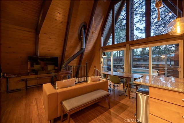 living room featuring high vaulted ceiling, a wood stove, plenty of natural light, and light wood-type flooring