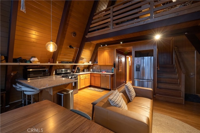 kitchen featuring sink, decorative light fixtures, stone counters, stainless steel appliances, and light hardwood / wood-style floors