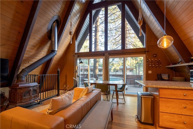 living room with high vaulted ceiling, wood walls, a wood stove, light wood-type flooring, and beam ceiling