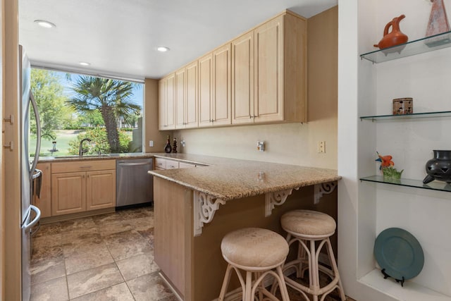 kitchen featuring light stone counters, sink, kitchen peninsula, a kitchen bar, and stainless steel appliances