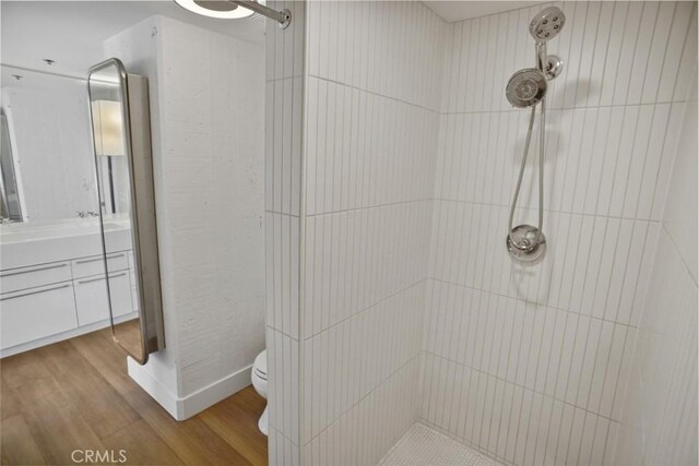 bathroom with a tile shower, hardwood / wood-style flooring, toilet, and vanity