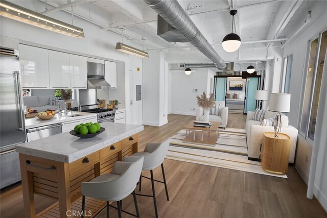 kitchen featuring light hardwood / wood-style floors, white cabinets, light stone countertops, high quality appliances, and wall chimney range hood