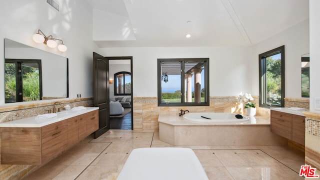 bathroom with lofted ceiling, vanity, tiled bath, and a wealth of natural light