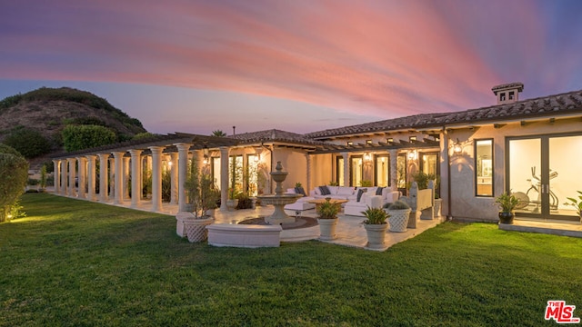 back house at dusk featuring a lawn and a patio