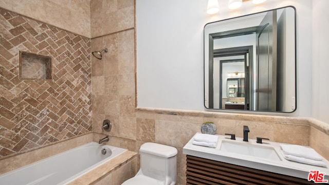 full bathroom with tile walls, tiled shower / bath combo, vanity, and toilet