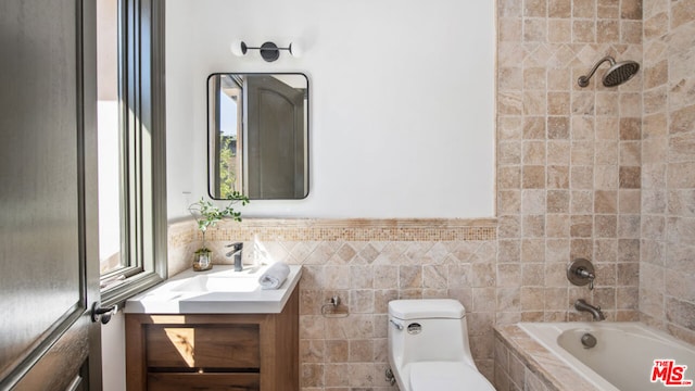 full bathroom featuring tile walls, tiled shower / bath, vanity, and toilet