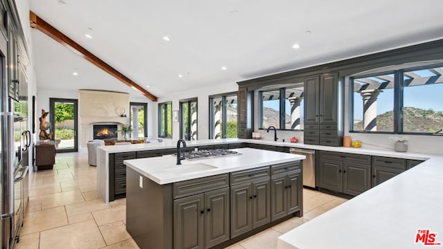 kitchen with a healthy amount of sunlight, vaulted ceiling with beams, and a kitchen island with sink