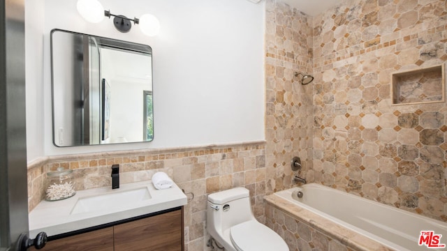 full bathroom featuring tiled shower / bath, vanity, tile walls, and toilet