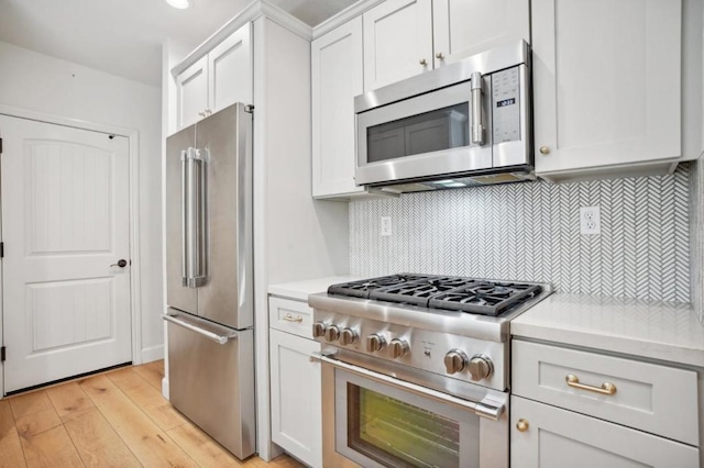 kitchen with high end appliances, tasteful backsplash, white cabinets, and light hardwood / wood-style flooring