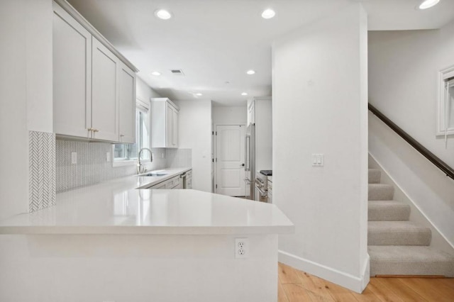 kitchen with white cabinetry, high end fridge, kitchen peninsula, and sink