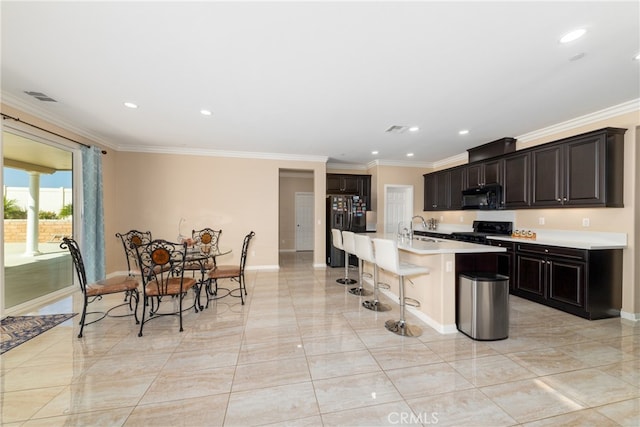 kitchen featuring an island with sink, black appliances, a kitchen breakfast bar, and crown molding