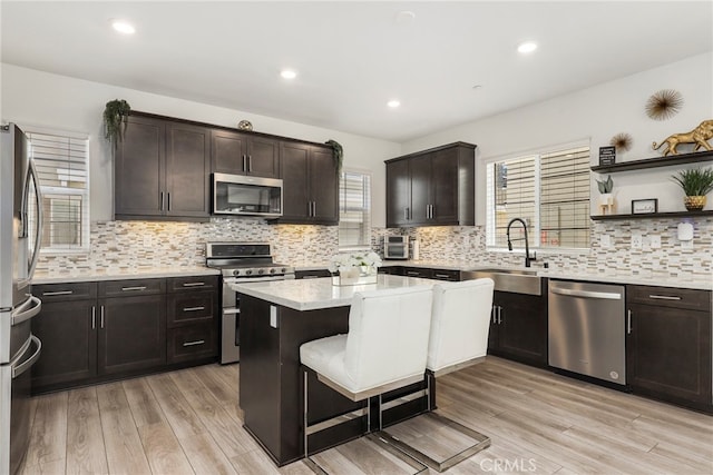 kitchen featuring appliances with stainless steel finishes, sink, light hardwood / wood-style floors, dark brown cabinetry, and decorative backsplash