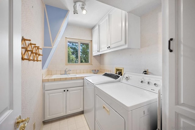 clothes washing area with washing machine and clothes dryer, cabinets, and sink