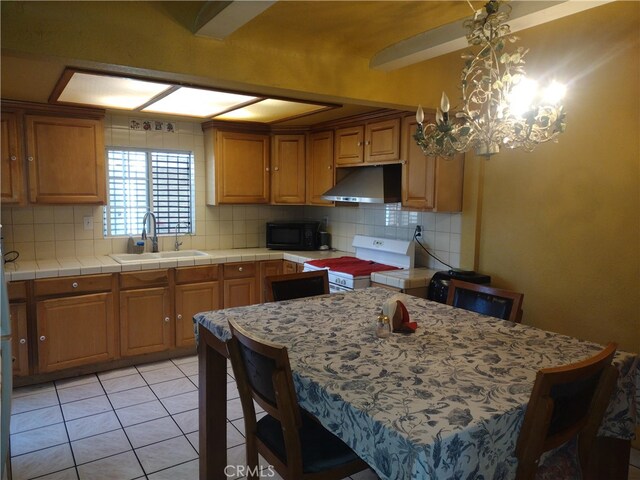 kitchen with light tile patterned floors, sink, backsplash, tile counters, and white range oven