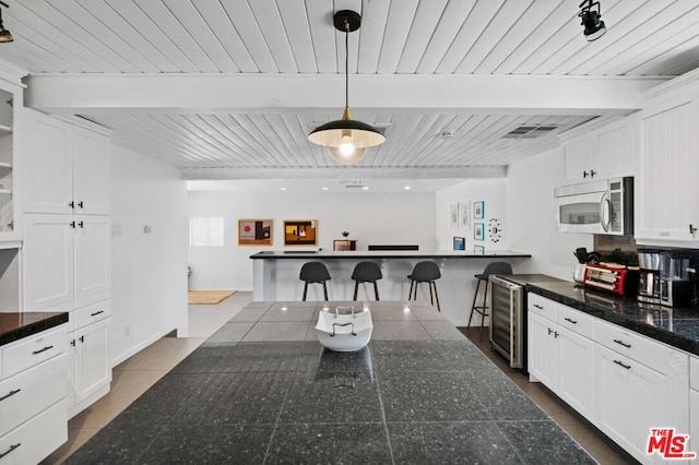 kitchen with wine cooler, beamed ceiling, hanging light fixtures, white cabinetry, and a kitchen breakfast bar