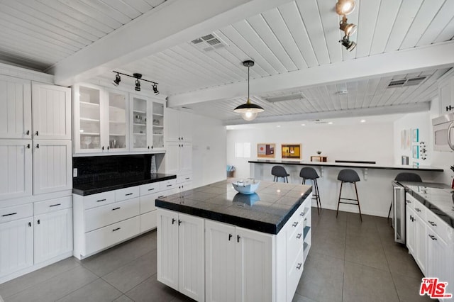 kitchen with a kitchen breakfast bar, hanging light fixtures, white cabinetry, beamed ceiling, and a center island