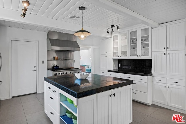 kitchen featuring beamed ceiling, a kitchen island, wall chimney exhaust hood, decorative light fixtures, and white cabinetry