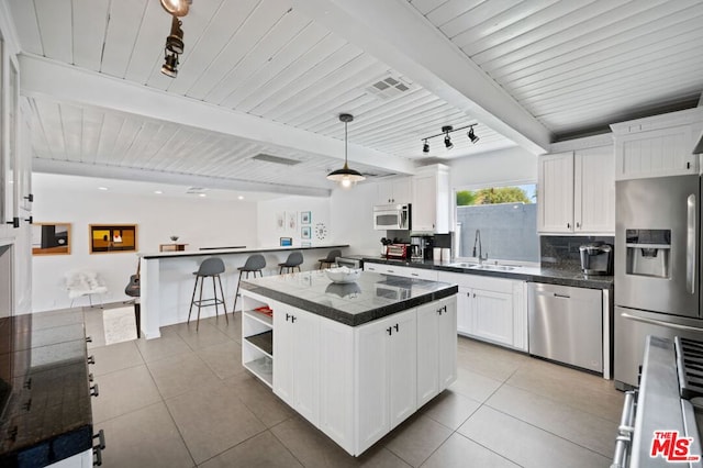 kitchen with pendant lighting, beamed ceiling, white cabinetry, appliances with stainless steel finishes, and a center island